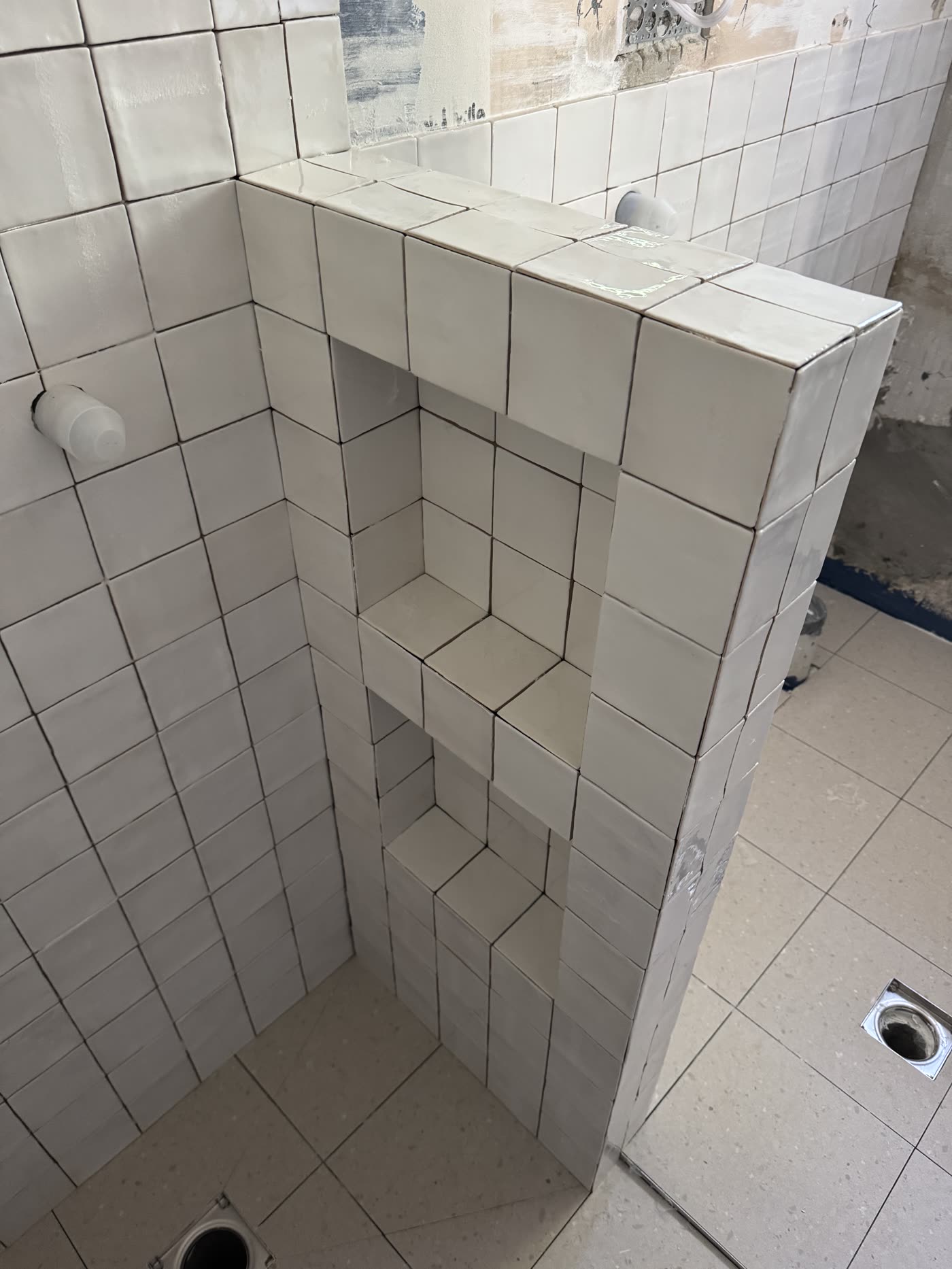 Square white tiling wrapped neatly around a shower niche and shelves