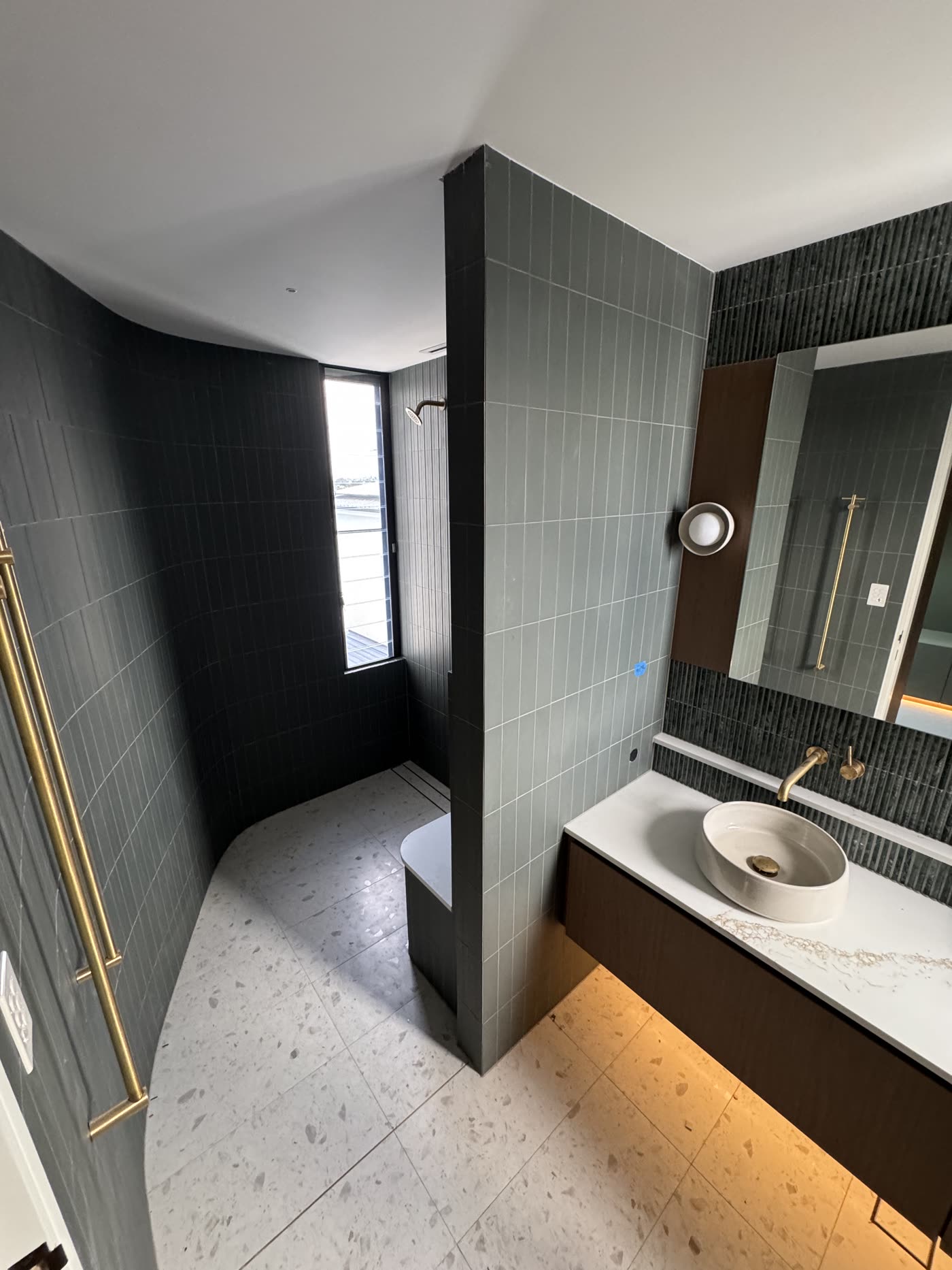 Dark ribbed wall tiling with terrazzo floor and brass tapware in a high-end bathroom