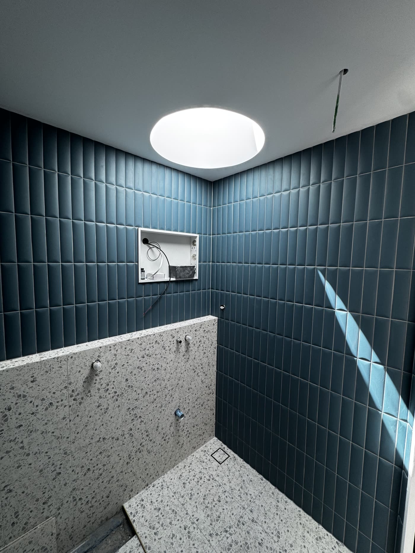 Deep teal vertical stack tiling with terrazzo bench and floor in a bathroom